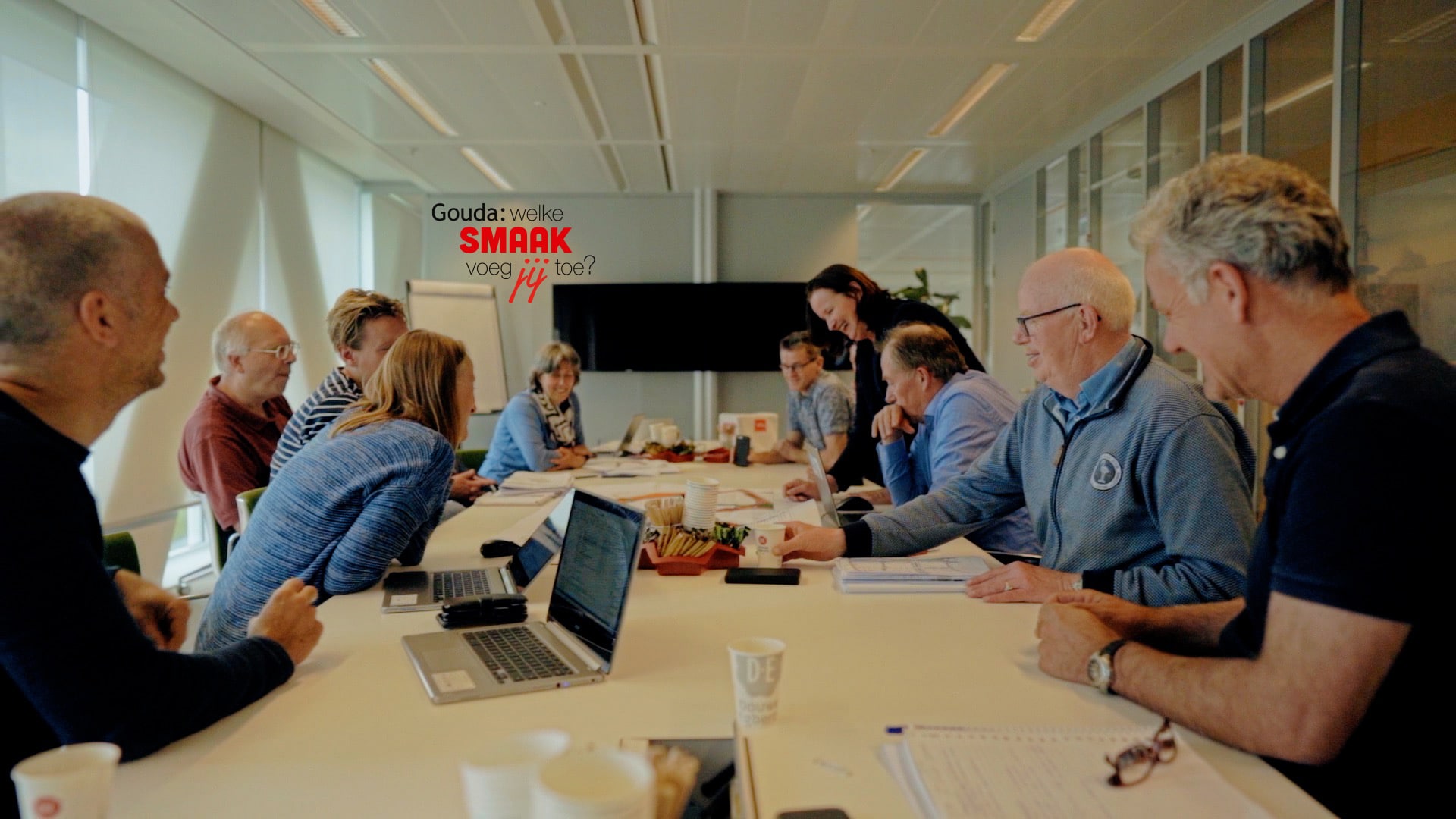 Overleg tussen collega Josy en haar collega's in een vergaderruimte in het Huis van de Stad. In het midden het logo Gouda: welke smaak voeg jij toe?